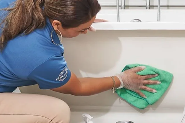Professional house cleaner wiping down a bathtub with a green microfiber cloth